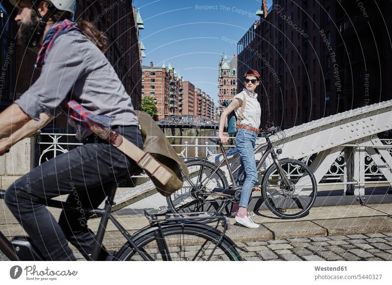Deutschland, Hamburg, Frau mit Elektrofahrrad beobachtet Mann, der mit dem Fahrrad vorbeifährt fahren E-Bike eBikes E-Bikes Elektrorad ansehen Fahrräder Räder