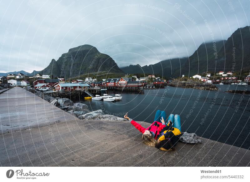 Norwegen, Lofoten, zwei junge Frauen liegen auf einem Pier an der Küste und machen ein Selfie Kueste Kuesten Küsten weiblich Landungssteg Piers Selfies liegend