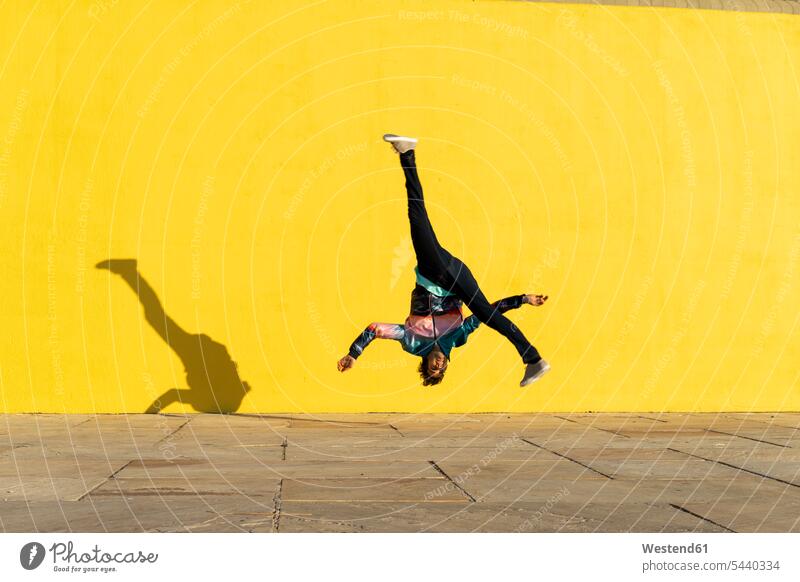 Akrobat springt Purzelbäume vor der gelben Wand Salto Saltos Salti gelber gelbes Akrobaten Mauer Mauern springen hüpfen Akrobatik Sport Sportler Wände Waende