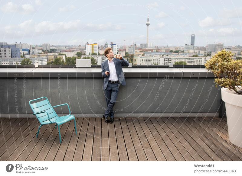 Deutschland, Berlin, Geschäftsmann bei einem Drink auf der Dachterrasse nach der Arbeit Businessmann Businessmänner Geschäftsmänner Dachterrassen Feierabend