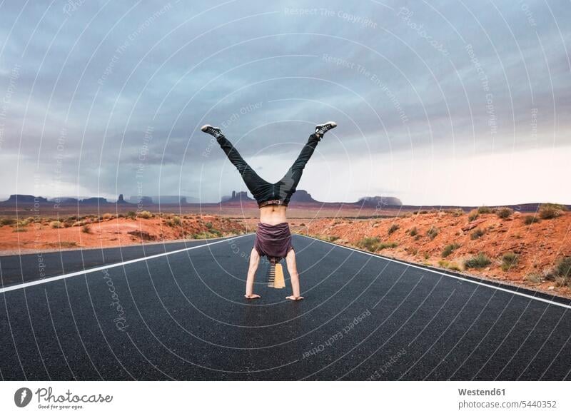 USA, Utah, Junger Mann macht Handstand auf der Straße zum Monument Valley kopfüber auf dem Kopf verkehrt herum junger Mann junge Männer Strassen Straßen stehen