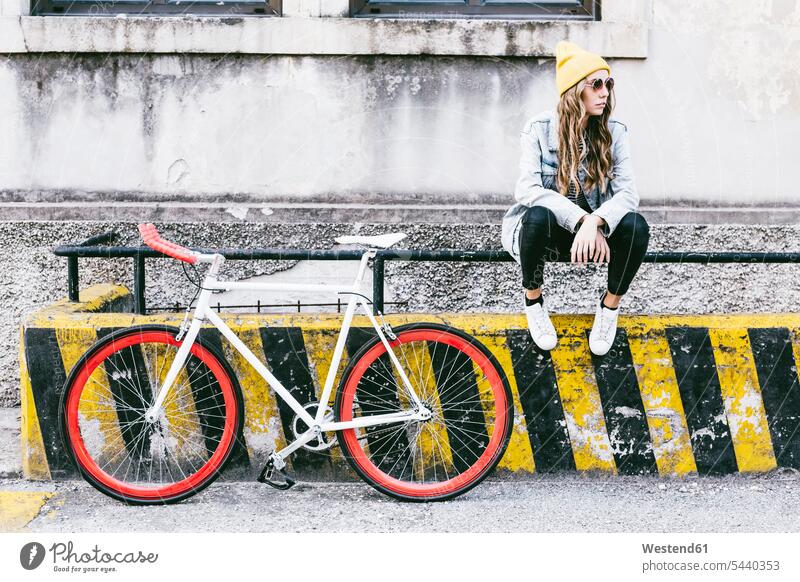 Modische junge Frau mit Fahrrad auf dem Geländer sitzend sitzt modisch Bikes Fahrräder Räder Rad weiblich Frauen Raeder Erwachsener erwachsen Mensch Menschen