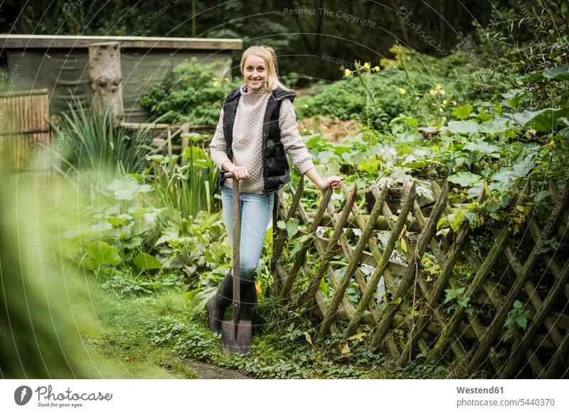 Porträt einer lächelnden jungen Frau mit Spaten im Garten weiblich Frauen Portrait Porträts Portraits Gärten Gaerten Gartenanlage Gartenanlagen Erwachsener