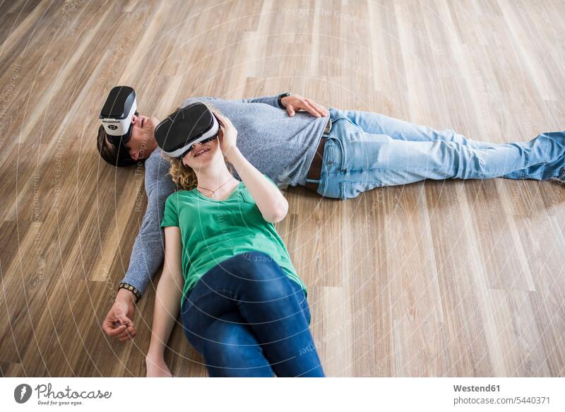 Junges Paar liegt auf dem Boden in leerer Wohnung und trägt VR-Brille Pärchen Paare Partnerschaft Virtual Reality Brille Virtual-Reality-Brille