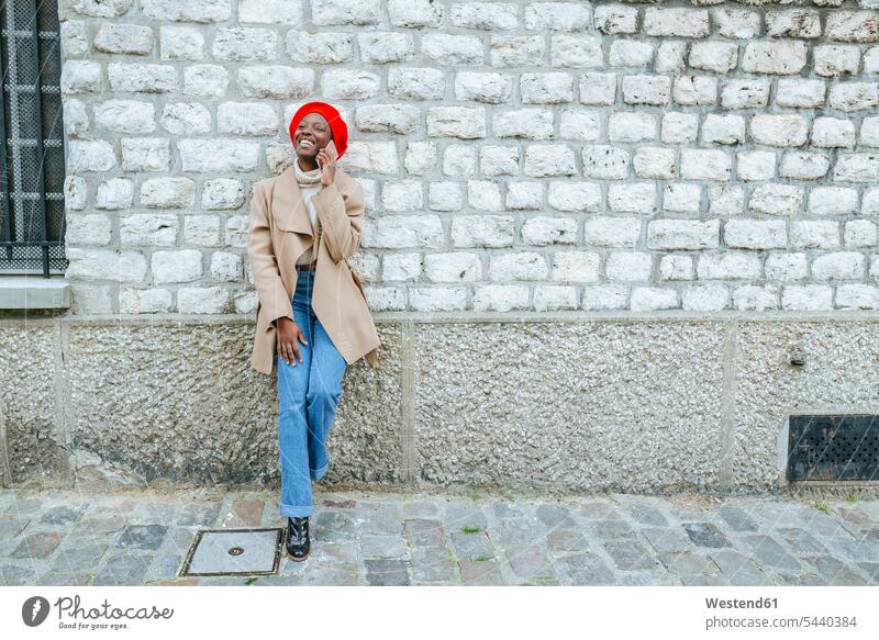Junge Frau in Paris lehnt an Wand und telefoniert weiblich Frauen Smartphone iPhone Smartphones telefonieren anrufen Anruf telephonieren lächeln alleinreisend
