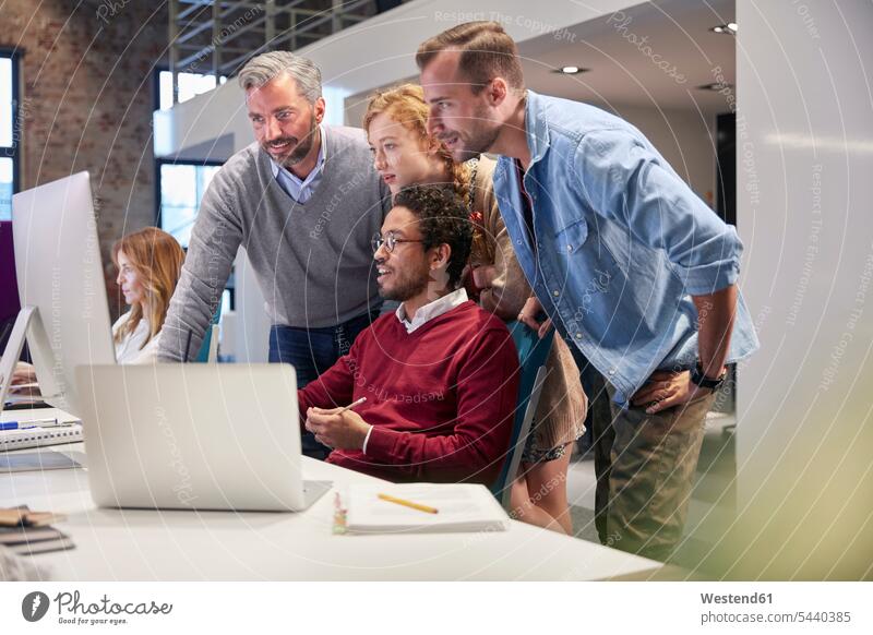 Kollegen schauen einem jungen Mann über die Schulter, der in einem modernen Büro arbeitet Team ansehen zuschauen Office Büros Kollegin Kolleginnen lächeln