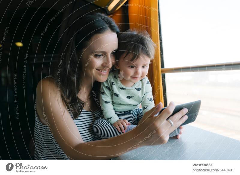 Glückliche Mutter und kleines Mädchen benutzen Smartphone während der Zugfahrt Mami Mutti Mütter Mama Handy Mobiltelefon Handies Handys Mobiltelefone Bahnen