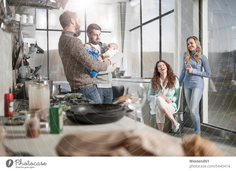 Zwei Ehefrauen beobachten Ehemänner, die ihre Babys in der Küche halten lächeln Freunde Küchen Familie Familien Vater Papas Väter Vati Vatis Papis Freundschaft