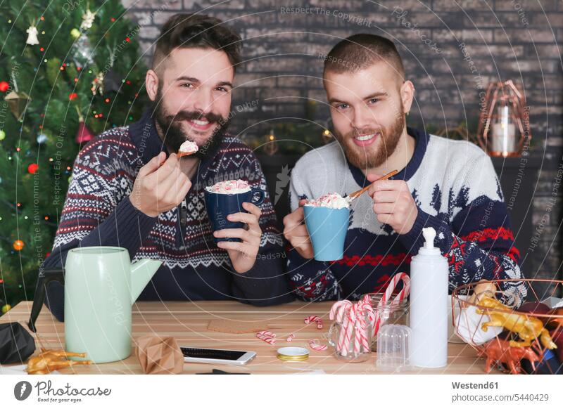 Glückliches schwules Paar trinkt zur Weihnachtszeit heiße Schokolade mit Sahne und gehackten Zuckerstangen Portrait Porträts Portraits Schwules Paar Schwuler