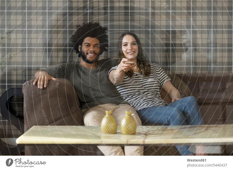 Lächelndes Paar sitzt auf der Couch und sieht fern Sofa Couches Liege Sofas Pärchen Paare Partnerschaft lächeln fernsehen Zuhause zu Hause daheim Mensch
