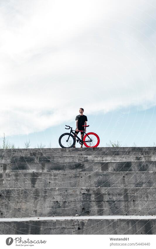 Junger Mann steht mit Fixie-Bike auf Betonstufen Männer männlich Fahrrad Bikes Fahrräder Räder Rad stehen stehend Stufen Treppe Treppenstufe Treppenstufen