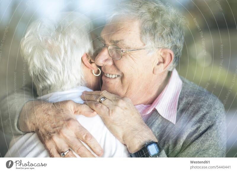 Glückliches älteres Paar umarmt sich hinter einer Fensterscheibe Fensterscheiben glücklich glücklich sein glücklichsein lächeln umarmen Umarmung Umarmungen
