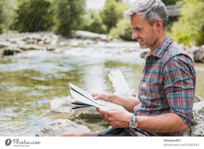 Wanderer sitzt am Flussufer und liest Karte Pause Karten wandern Wanderung Fluesse Fluß Flüsse Mann Männer männlich Gewässer Wasser Erwachsener erwachsen Mensch