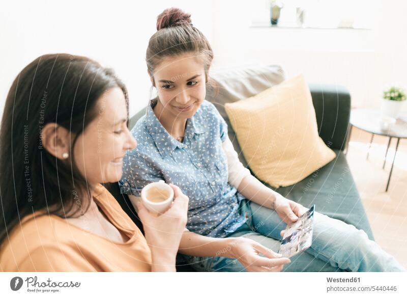 Mutter und erwachsene Tochter sitzen zu Hause auf der Couch und schauen sich Fotos an Mami Mutti Mütter Mama Töchter Sofa Couches Liege Sofas Familie Familien
