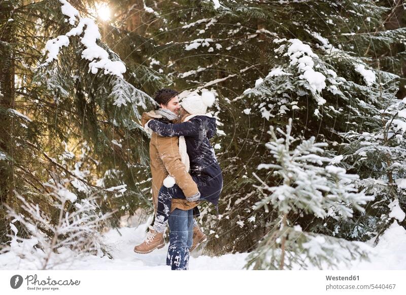 Glückliches junges Paar von Angesicht zu Angesicht im schneebedeckten Winterwald Pärchen Paare Partnerschaft Mensch Menschen Leute People Personen hochhalten