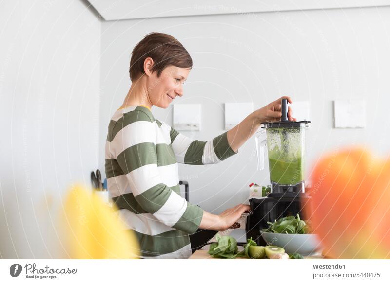 Lächelnde Frau bereitet grünen Smoothie in der Küche zu weiblich Frauen Portrait Porträts Portraits Smoothies Erwachsener erwachsen Mensch Menschen Leute People