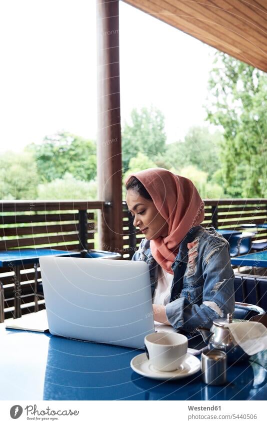 Junge Frau mit Hijab, die mit ihrem Laptop auf der Terrasse eines Cafés lernt muslimisch Moslem Muslim weiblich Frauen Notebook Laptops Notebooks Cafe