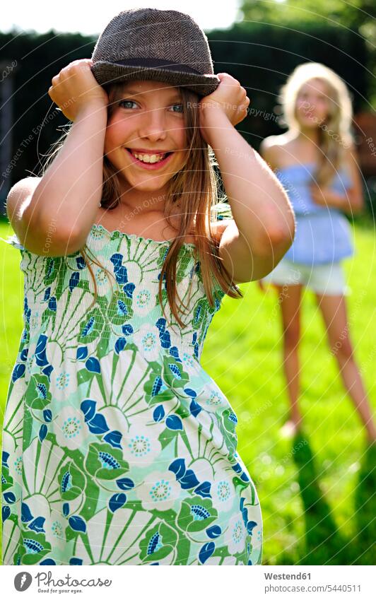 Fröhlich verspieltes Mädchen setzt im Garten einen Hut auf weiblich Gärten Gaerten lächeln Hüte Spaß Spass Späße spassig Spässe spaßig Kind Kinder Kids Mensch