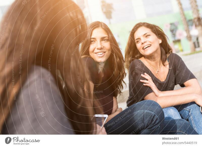 Drei glückliche junge Frauen sitzen im Freien Freundinnen lächeln Spaß Spass Späße spassig Spässe spaßig Freunde Freundschaft Kameradschaft weiblich sitzend