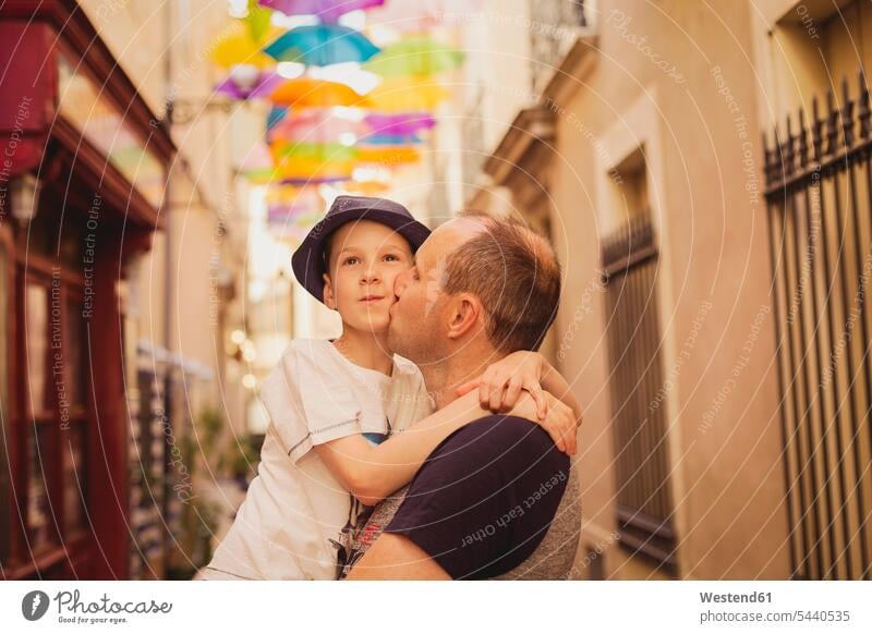 Frankreich, Languedoc, Beziers, Vater küsst Sohn mit bunten Regenschirmen im Hintergrund küssen Küsse Kuss Papas Väter Vati Vatis Papis Söhne Eltern Familie