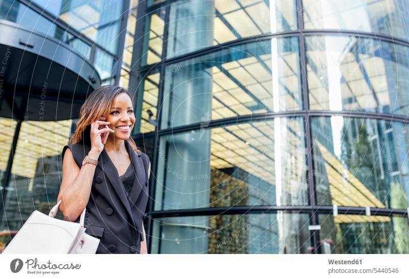 Lächelnde Frau am Telefon vor einem Bürogebäude in der Stadt lächeln Handy Mobiltelefon Handies Handys Mobiltelefone telefonieren anrufen Anruf telephonieren