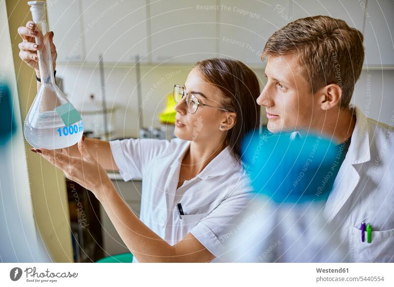 Junger Mann und Frau betrachten Flüssigkeit in Kolben im Labor ansehen Männer männlich Glaskolben Labore Flüssigkeiten flüssig Gemeinsam Zusammen Miteinander