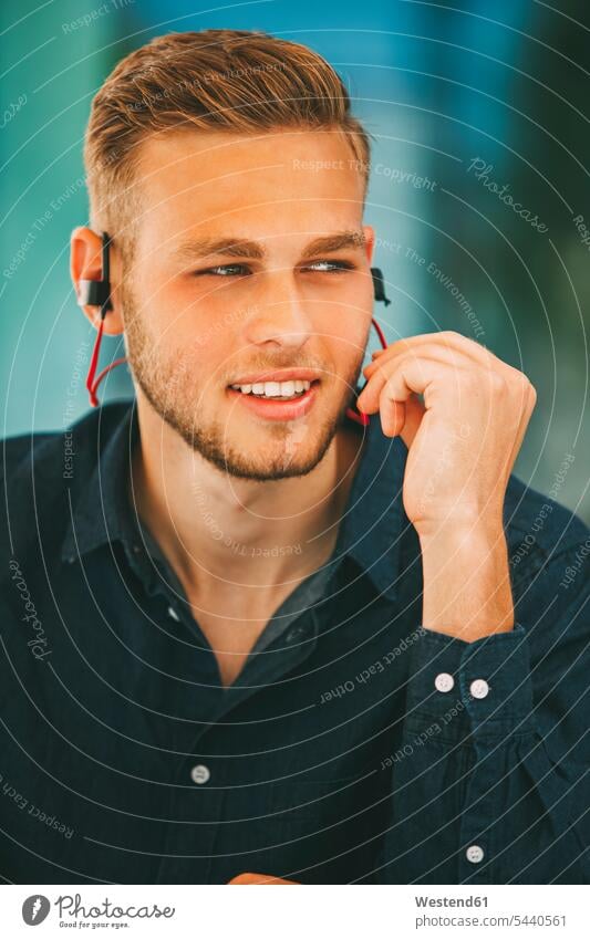 Junger Mann trägt Kopfhörer im Freien Männer männlich Ohrhörer Kopfhoerer Erwachsener erwachsen Mensch Menschen Leute People Personen In-Ear hören hoeren