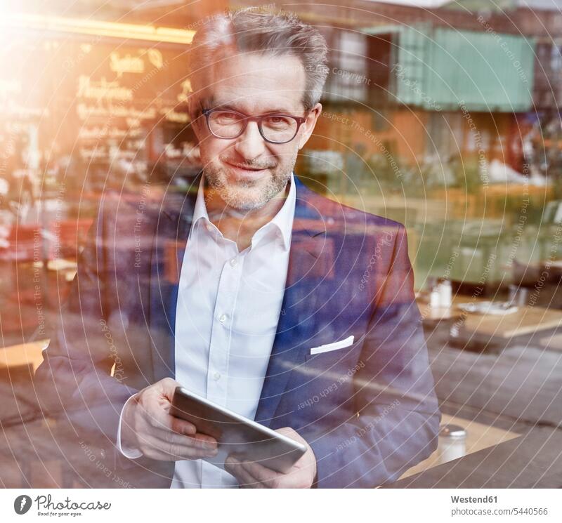 Selbstbewusster, reifer Geschäftsmann mit aus dem Fenster schauendem Tablett lächeln Tablet Computer Tablet-PC Tablet PC iPad Tablet-Computer Businessmann