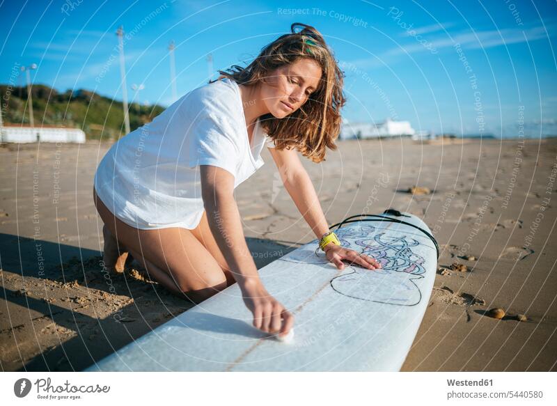Junge Frau trägt am Strand Paraffin auf einem Surfbrett auf weiblich Frauen Surfbretter surfboard surfboards Erwachsener erwachsen Mensch Menschen Leute People