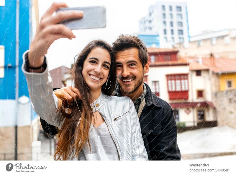 Ein lächelndes Paar macht ein Selfie in der Stadt Pärchen Paare Partnerschaft Selfies Handy Mobiltelefon Handies Handys Mobiltelefone Mensch Menschen Leute
