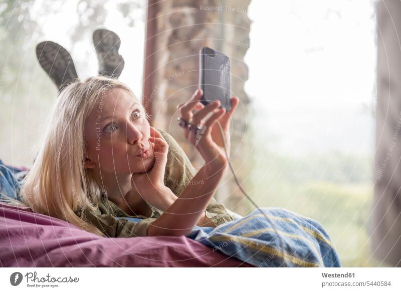 Porträt einer jungen Frau auf dem Bett liegend, die ein Selfie mit ihrem Handy macht Smartphone iPhone Smartphones Selfies weiblich Frauen Mobiltelefon Handies