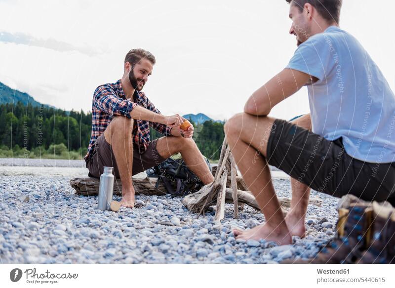 Deutschland, Bayern, zwei Wanderer rasten am Lagerfeuer auf einer Kiesbank Freunde Freundschaft Kameradschaft sitzen sitzend sitzt Schotterbank barfuß