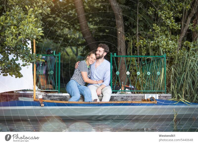 Glückliches junges Paar mit Kanu auf einem Steg sitzend Kanus Pärchen Paare Partnerschaft Stege Anlegestelle glücklich glücklich sein glücklichsein sitzt