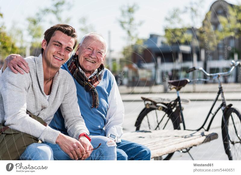 Porträt eines glücklichen älteren Mannes mit erwachsenem Enkel, der auf einer Bank sitzt Glück glücklich sein glücklichsein sitzen sitzend lächeln Enkelsöhne