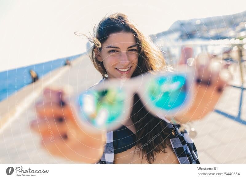 Junge Frau in Strandbekleidung mit Sonnenbrille junge Frau junge Frauen Bikini Bikinis Sonnenbrillen Brille halten weiblich Erwachsener erwachsen Mensch