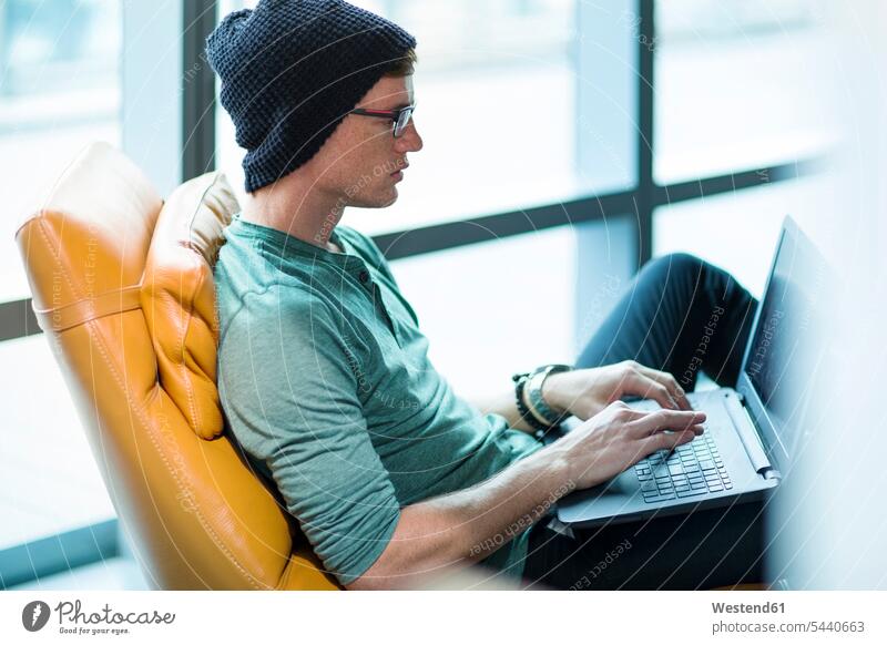 Junger Mann arbeitet im Sessel, benutzt Laptop arbeiten Arbeit Männer männlich sitzen sitzend sitzt Notebook Laptops Notebooks Konzentration konzentriert