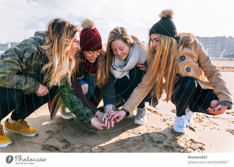 Vier Freunde reichen sich am Strand die Hände Freundinnen Beach Straende Strände Beaches Freundschaft Kameradschaft Hand hocken kauernd hockend verbinden Mensch