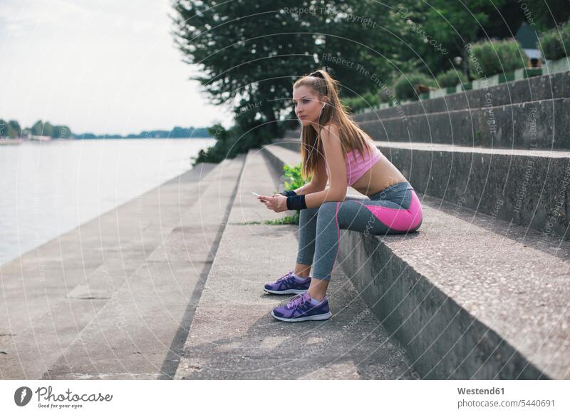 Sportliche Frau macht eine Pause am Flussufer trainieren sportlich sitzen sitzend sitzt weiblich Frauen Erwachsener erwachsen Mensch Menschen Leute People