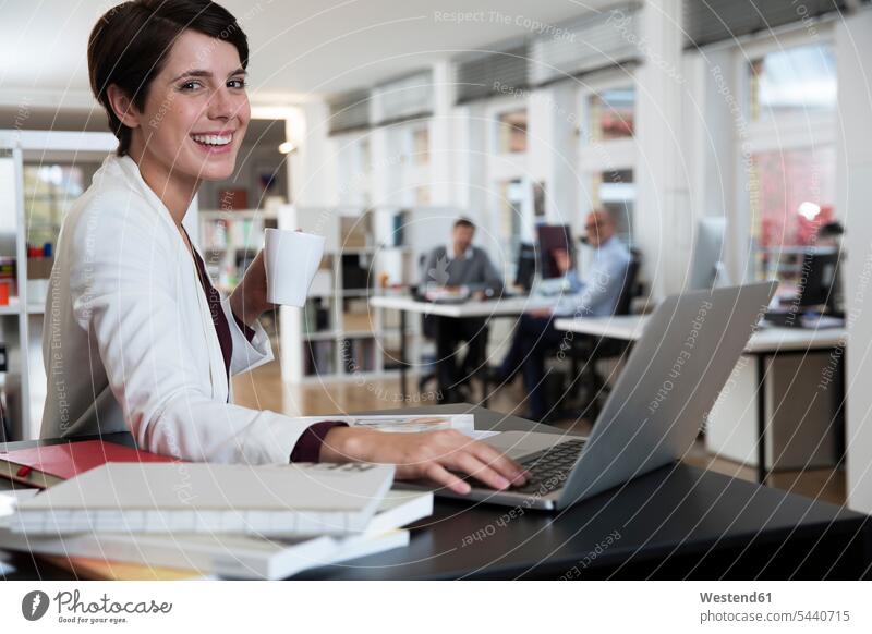 Portrait einer glücklichen Frau mit Laptop im Büro mit Kollegen im Hintergrund lächeln Geschäftsfrau Geschäftsfrauen Businesswomen Businessfrauen Businesswoman