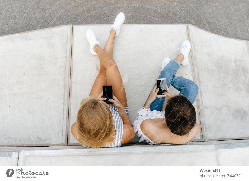 Zwei junge Frauen benutzen Mobiltelefone in einem Skatepark Freundinnen Handy Handies Handys Skateboardpark Skateboard-Park Skateboard Park Skaterplatz weiblich
