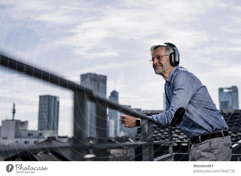 Grauhaariger Mann mit Kopfhörern genießt Stadtansicht Pause Geschäftsmann Businessmann Businessmänner Geschäftsmänner hören hoeren Musik Kopfhoerer entspannt