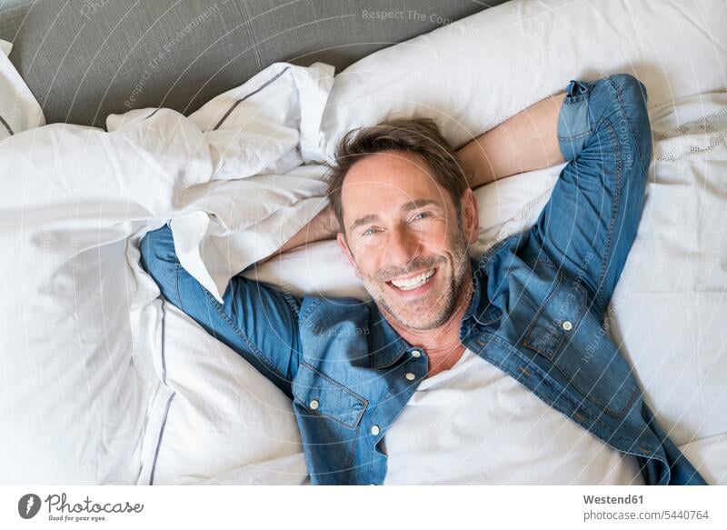 Porträt eines glücklichen reifen Mannes auf dem Bett liegend mit Händen hinter dem Kopf Männer männlich Betten Portrait Porträts Portraits Erwachsener erwachsen