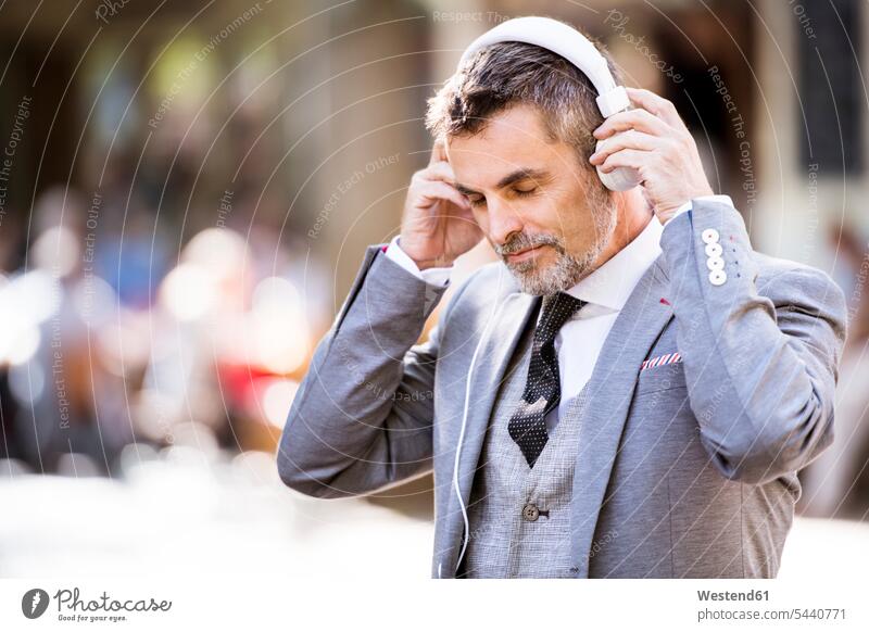 Älterer Geschäftsmann mit Kopfhörern in der Stadt hören hoeren Mann Männer männlich Kopfhoerer staedtisch städtisch Erwachsener erwachsen Mensch Menschen Leute