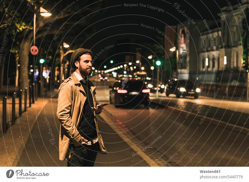 Stylischer junger Mann mit Handy auf nächtlicher Stadtstraße Männer männlich Nacht nachts Mobiltelefon Handies Handys Mobiltelefone Erwachsener erwachsen Mensch