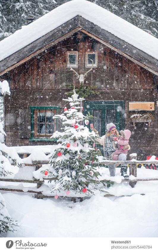 Österreich, Altenmarkt-Zauchensee, Mutter mit kleinem Sohn schmückt Weihnachtsbaum am Holzhaus Schnee Winter winterlich Winterzeit Familie Familien Mami Mutti