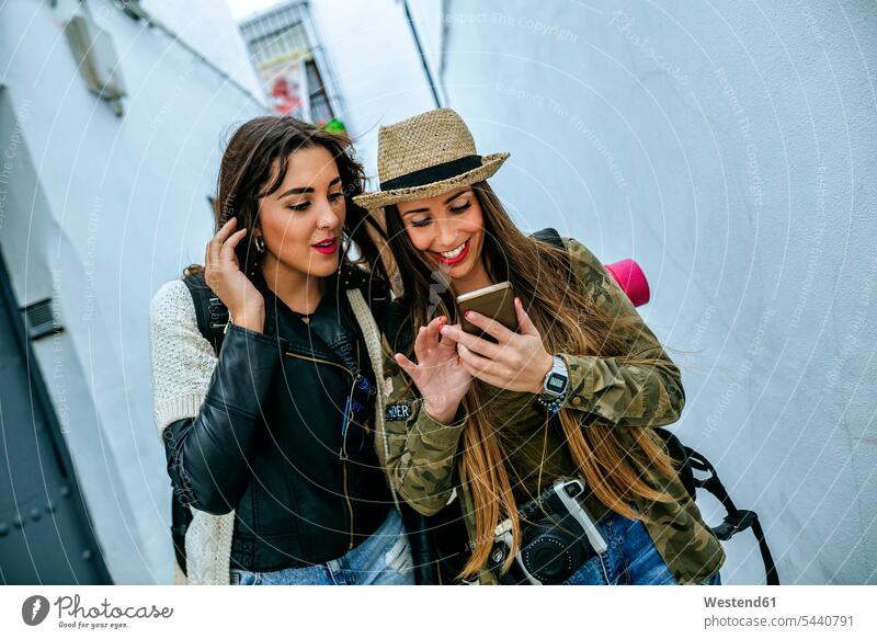 Zwei junge Frauen in einer Stadt, die sich ein Handy anschauen Freundinnen Mobiltelefon Handies Handys Mobiltelefone lächeln Freunde Freundschaft Kameradschaft