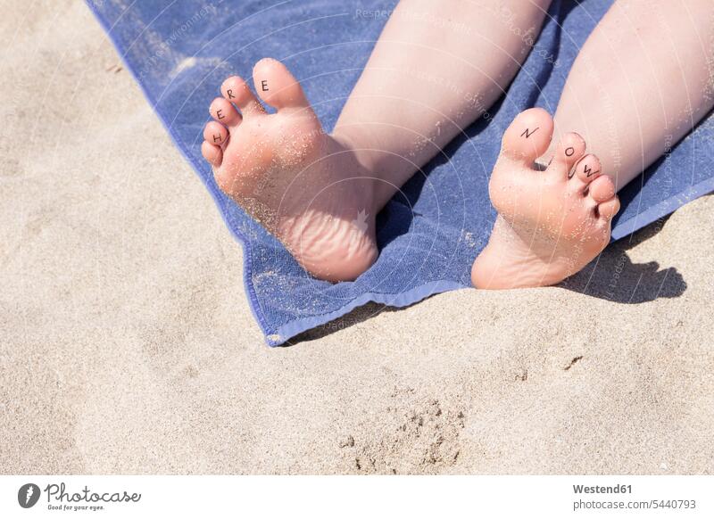 Füße einer Frau mit der Schrift 'Here Now' an den Zehen Strand Beach Straende Strände Beaches Fuß Fuss Mensch Menschen Leute People Personen Ferien Handtuch