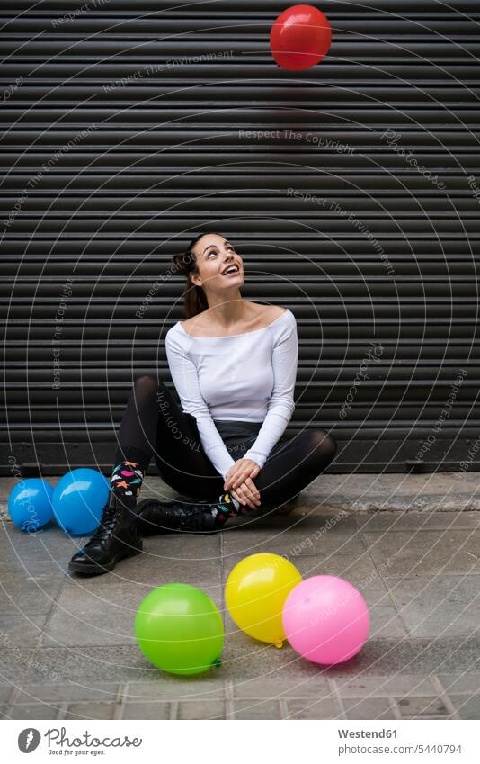Junge Frau sitzt auf dem Bürgersteig und schaut zu, wie ein Ballon fliegt Luftballon Luftballons Ballons Luftballone weiblich Frauen Erwachsener erwachsen