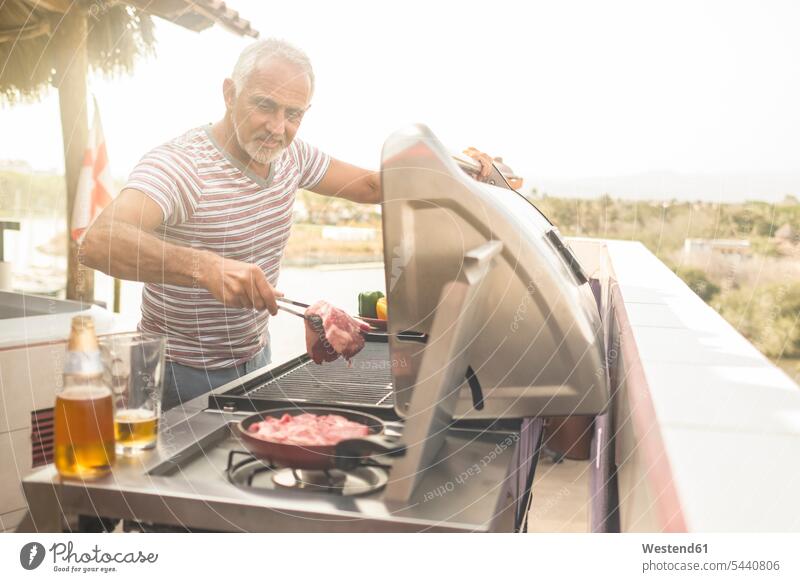 Reifer Mann grillt Steaks auf einem Gasgrill auf seiner Penthouse-Terrasse grillen Männer männlich lächeln Erwachsener erwachsen Mensch Menschen Leute People