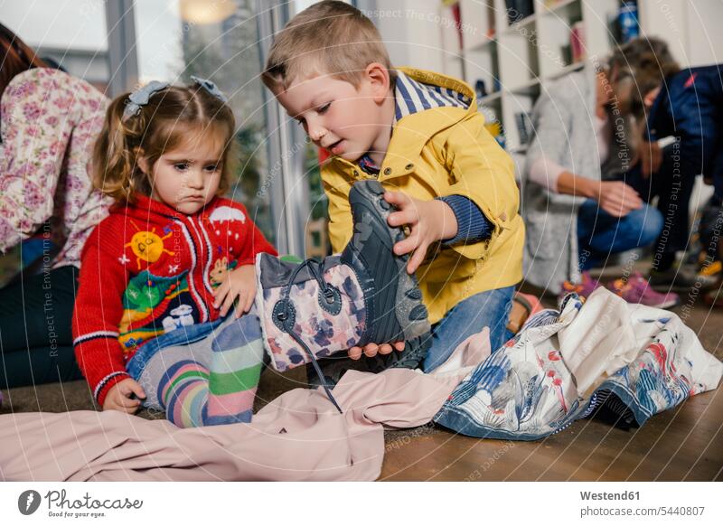 Junge hilft Mädchen beim Anziehen ihrer Stiefel im Kindergarten Kids Kindergaerten Kindergärten helfen mithelfen Hilfsbereitschaft beistehen Mithilfe Beistand